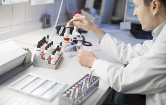 Midsection of doctor collecting medical samples in test tube. High angle view of male scientist is working at laboratory. He is sitting at table in hospital.